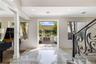 Foyer featuring large-format light-toned stone flooring, decorative iron stair railing, recessed ceiling lighting, and expansive square-cased entry to