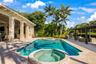 Swimming pool with integrated spa, covered lanai featuring structural columns, paver decking, and metal pergola