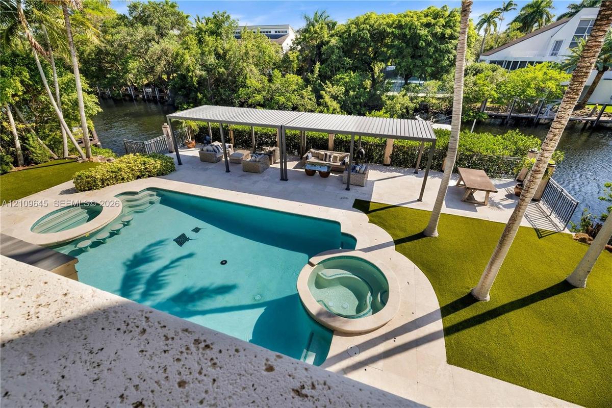 Waterfront backyard featuring a swimming pool with integrated spa, paved patio area, metal-frame pergola, and artificial turf lawn