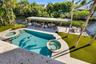 Waterfront backyard featuring a swimming pool with integrated spa, paved patio area, metal-frame pergola, and artificial turf lawn