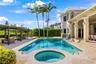Outdoor pool with an integrated spa, stone-paver pool deck, covered patio with structural columns, and a detached metal-frame pergola