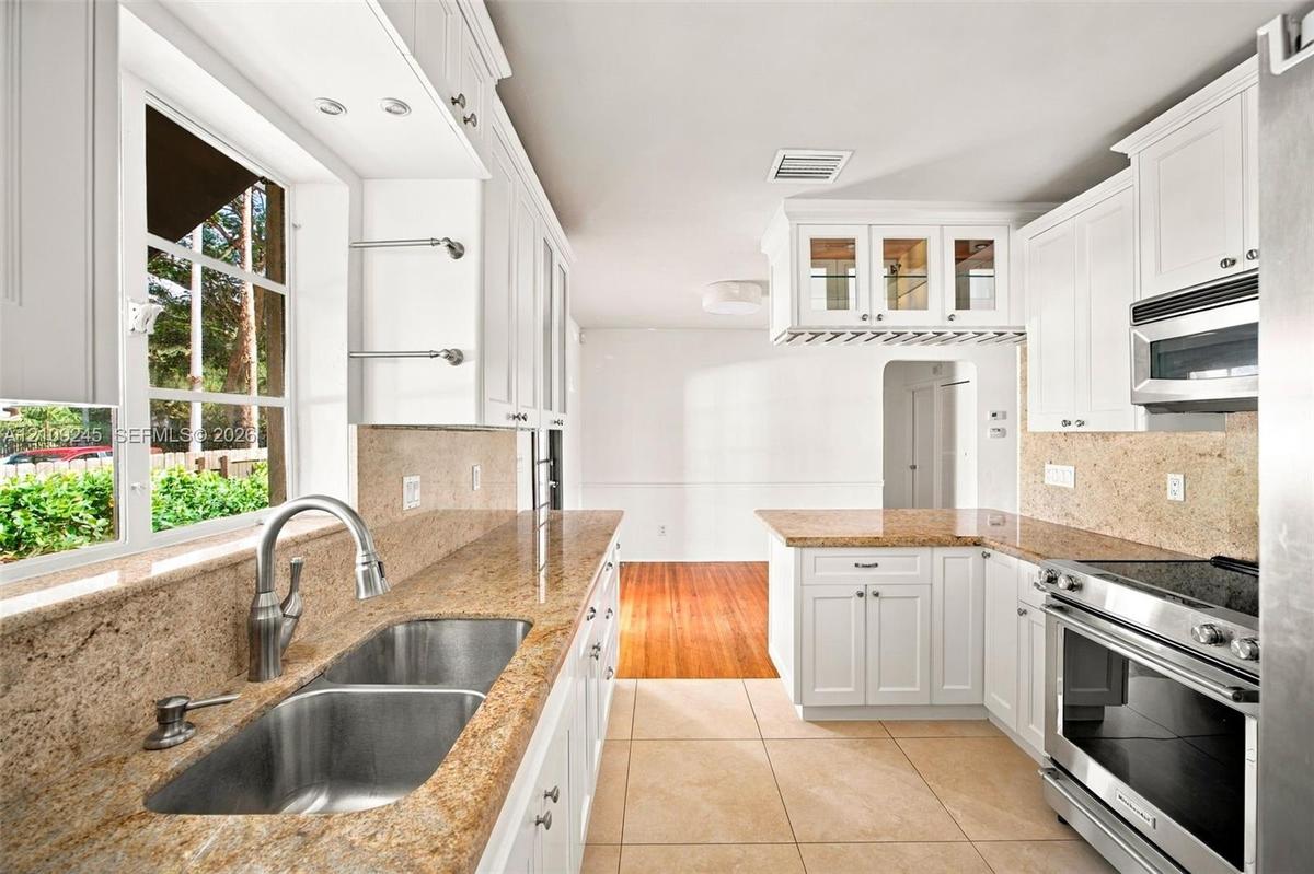 Kitchen featuring white cabinetry, stone countertops, a dual-basin stainless steel sink with a high-arch faucet, built-in stainless steel appliances, 