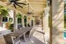Covered outdoor kitchen and dining area featuring a stone-tile patio, built-in stainless steel range hood, stone-clad counter, multi-blade ceiling fan