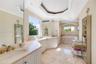 Bathroom featuring stone-finish flooring, white built-in cabinetry with stone countertops, an inset soaking tub with a stone surround, and an octagona