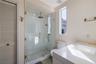 Walk-in glass shower featuring a rain-style showerhead and handheld sprayer with brass hardware, complemented by a white vanity with a rectangular int