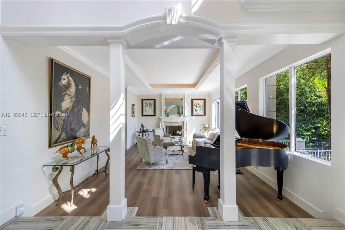 Open floor plan featuring wood-finish flooring, tray ceilings, a central stone-surround fireplace, and large picture windows