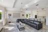 Open-concept area featuring high-gloss cabinetry, stone tile flooring, tray ceilings, recessed lighting, and a kitchen island with integrated sink