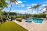 Rear yard featuring a pool with an integrated spa, stone-finish decking, a metal pergola, and synthetic turf lawn