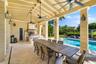Covered outdoor patio featuring stone flooring, vaulted beamed ceiling with multiple ceiling fans, built-in kitchen with stainless steel range hood, a
