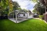 Backyard featuring a concrete-pad carport, synthetic turf lawn, dark wood-finish privacy fencing, and mature palm trees