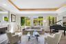 Living area featuring tray ceilings, wood-finish flooring, and a fireplace with a detailed mantel, illuminated by large windows