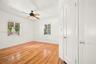 Interior room featuring wood-finish flooring, two windows with blinds, a ceiling fan with integrated lighting, and a white paneled door
