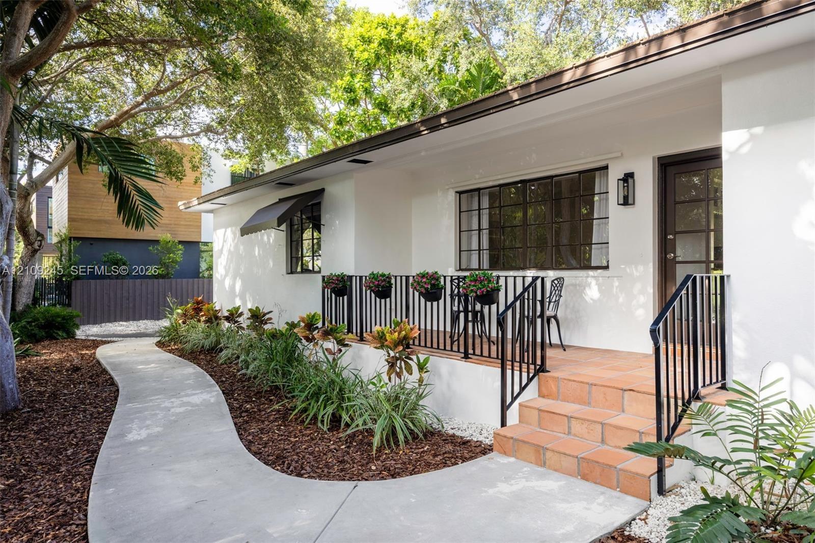 Exterior featuring white stucco siding, a terracotta-tiled front porch, black metal railings, and a curved concrete walkway