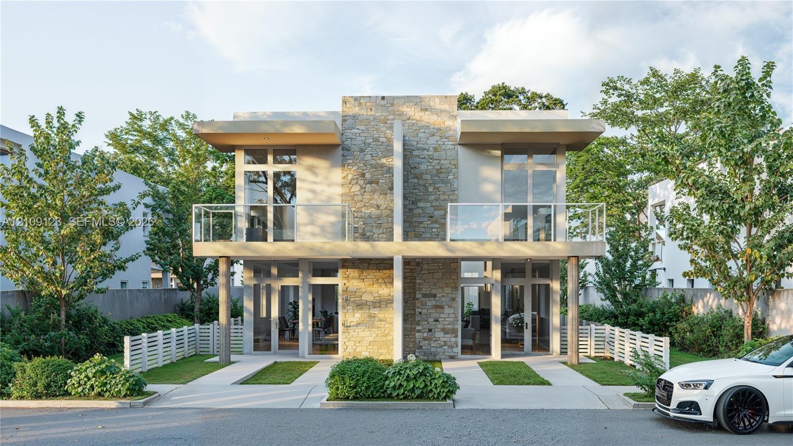 Modern two-story architectural design featuring a natural stone facade, dual upper-level balconies with glass railings, floor-to-ceiling windows, and 