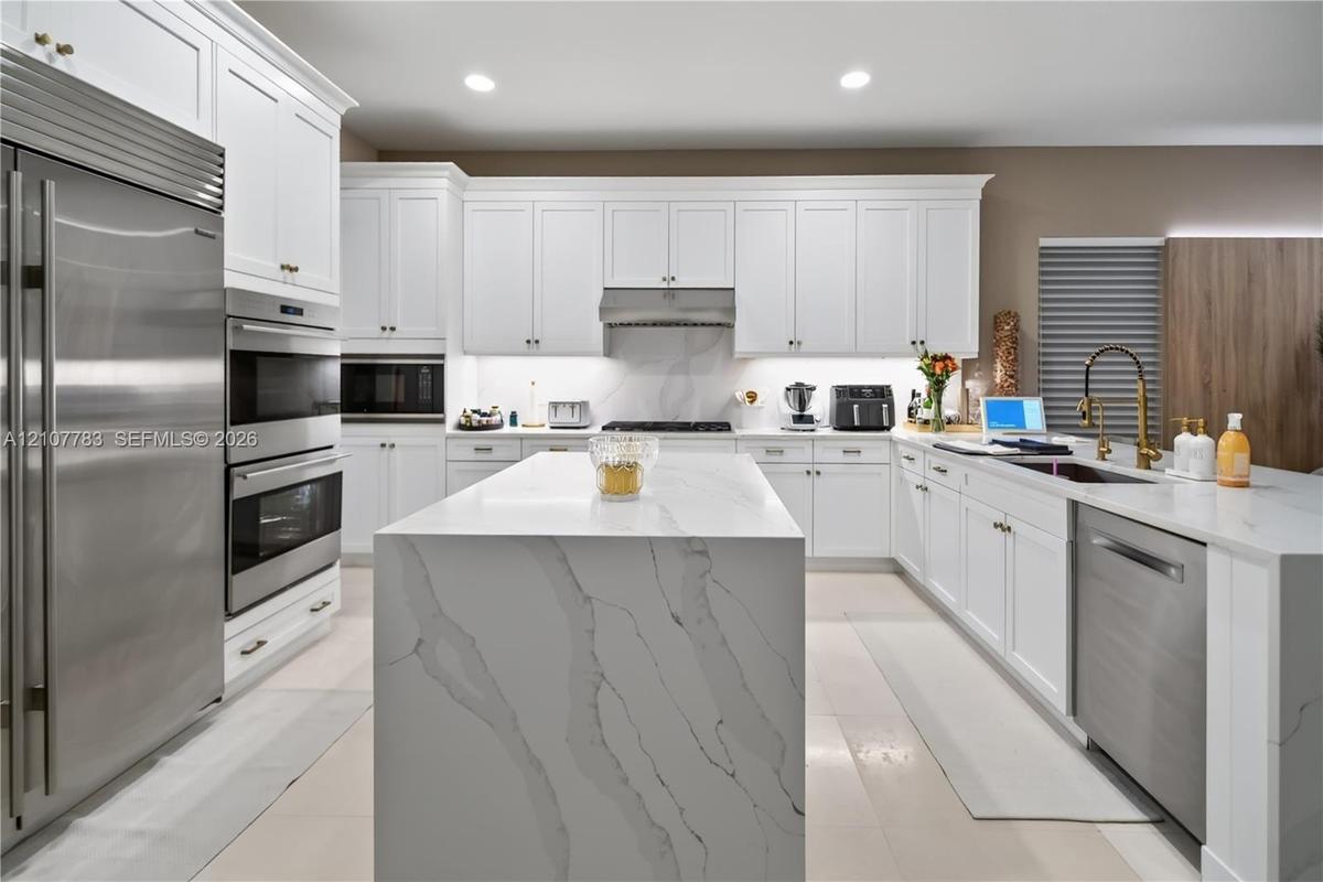 Kitchen featuring white shaker cabinetry, a waterfall-edge center island with stone-finish countertops, stainless steel appliances, a professional-sty