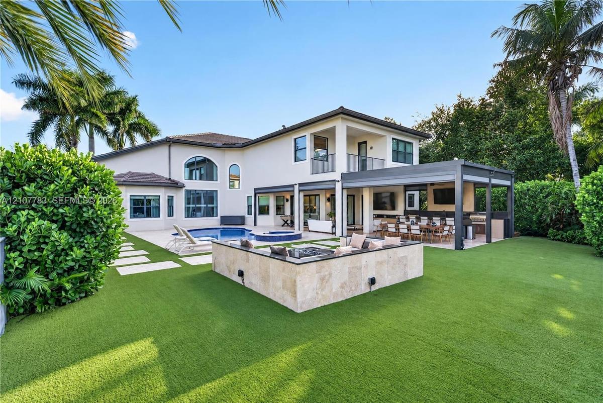 Rear exterior featuring a swimming pool, integrated spa, covered patio with outdoor kitchen, and stone-clad fire feature