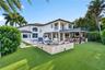 Rear exterior featuring a swimming pool, integrated spa, covered patio with outdoor kitchen, and stone-clad fire feature