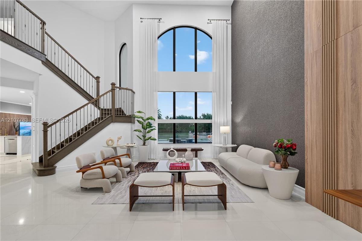 Two-story great room featuring a double-height arched window, floor-to-ceiling textured accent wall, wood-paneled wall detail, and a staircase with wr