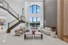 Two-story great room featuring a double-height arched window, floor-to-ceiling textured accent wall, wood-paneled wall detail, and a staircase with wr