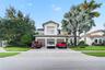 Two-story stucco exterior featuring a three-car garage, paver driveway, and mature palm landscaping