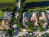 Aerial perspective of a property featuring a swimming pool, attached spa, paver driveway, and mature palm trees situated along a waterway