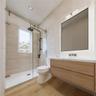 Floating wood-finish vanity with countertop, glass-enclosed shower with matte black fixtures, and recessed lighting
