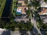 Aerial perspective of a waterfront property featuring a multi-pitched tiled roof, private swimming pool, concrete paver patio, and professional landsc