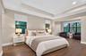Bedroom featuring wood-finish flooring, a tiered tray ceiling, and multiple windows with roller shades