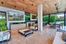 Covered outdoor living space featuring natural stone flooring, wood-plank ceiling, recessed lighting, and a built-in outdoor kitchen with stone counte