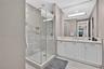 Walk-in glass shower with tile surround, white cabinetry, integrated sink, stone-finish countertop, and large vanity mirror