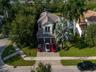Aerial perspective of a multi-story residence featuring a tile roof, three-car garage, and a paved stone driveway situated on a landscaped lot with ma