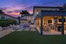 Rear exterior featuring a covered patio with a built-in outdoor kitchen, a swimming pool with an integrated spa, stone-paver hardscaping, and syntheti