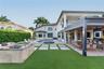 Outdoor living area featuring a covered pergola, stone-clad fire pit, swimming pool with attached spa, and artificial turf lawn with stone pavers