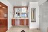 Floating curved wood-finish vanity with dual integrated sinks, stone-surface countertop, full-width mirror, and glass-enclosed shower