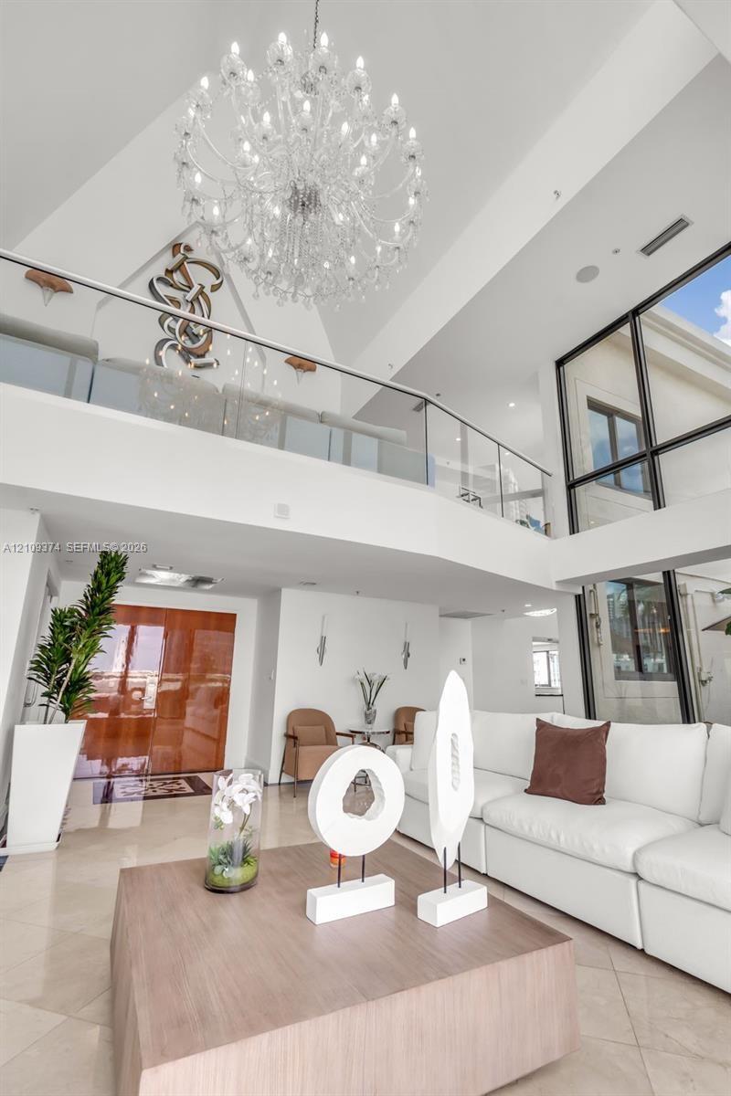 Two-story foyer featuring vaulted ceilings, floor-to-ceiling windows, a large multi-tiered crystal chandelier, and a glass-paneled mezzanine railing