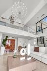 Two-story foyer featuring vaulted ceilings, floor-to-ceiling windows, a large multi-tiered crystal chandelier, and a glass-paneled mezzanine railing