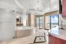 Soaking tub with stone surround, glass-enclosed shower, expansive vanity with stone countertop, ornate chandelier, and polished tile flooring with geo