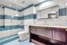 Bathroom featuring a glass-enclosed shower, wood-finish vanity with stone countertop, integrated undermount sink, and multi-tone horizontal wall tilin