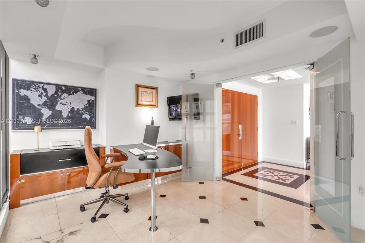 Light-filled room featuring large-format stone flooring with decorative inlay, custom wood-finish built-in cabinetry, frosted glass pivot entry doors,