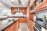 Kitchen featuring warm-toned cabinetry, expansive stone countertops, built-in stainless steel appliances, a professional-style range hood, and track l