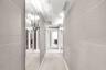 Hallway featuring large-format light-toned wall tile, floor-to-ceiling mirror panels, and dual metallic wall-mounted sconces
