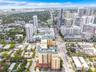 Aerial perspective of a multi-story urban complex featuring a prominent peaked roofline, stucco-finish facade, ground-level parking access, and extens