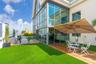 Expansive rooftop terrace featuring floor-to-ceiling glass wall panels, synthetic turf lawn, wood-finish decking, and light-colored stucco exterior si