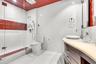 Bathroom featuring a glass-enclosed shower with multi-head fixtures and decorative tile accents, a curved wood-finish vanity with a vessel sink, and a