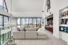 Vaulted ceilings with floor-to-ceiling windows, crystal chandelier, built-in horizontal wood-slat cabinetry, and integrated glass shelving