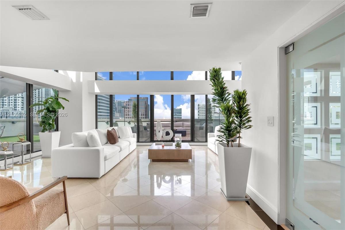 Expansive living area featuring floor-to-ceiling windows, polished stone flooring, and a glass-panel door
