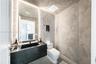 Bathroom featuring textured wall finishes, a floating black countertop with an integrated basin, vertical recessed LED lighting, and mosaic-tiled acce