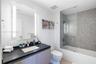 Vanity with a dark countertop and integrated rectangular sink, wood-finish cabinetry, illuminated mirror, and a tiled shower-tub combination with a gl