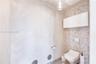 Wall-mounted toilet with a dual-flush actuator plate, mosaic tile accent wall, wall-mounted storage cabinet, and glass pendant lighting