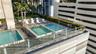 Rooftop terrace featuring multiple swimming pools, tiered hardscaping, manicured hedges, and glass perimeter railings